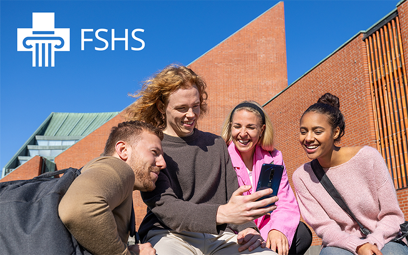 Four students spend time in the campus yard, looking happy and looking at a cell phone together; the image also shows the FSHS logo.